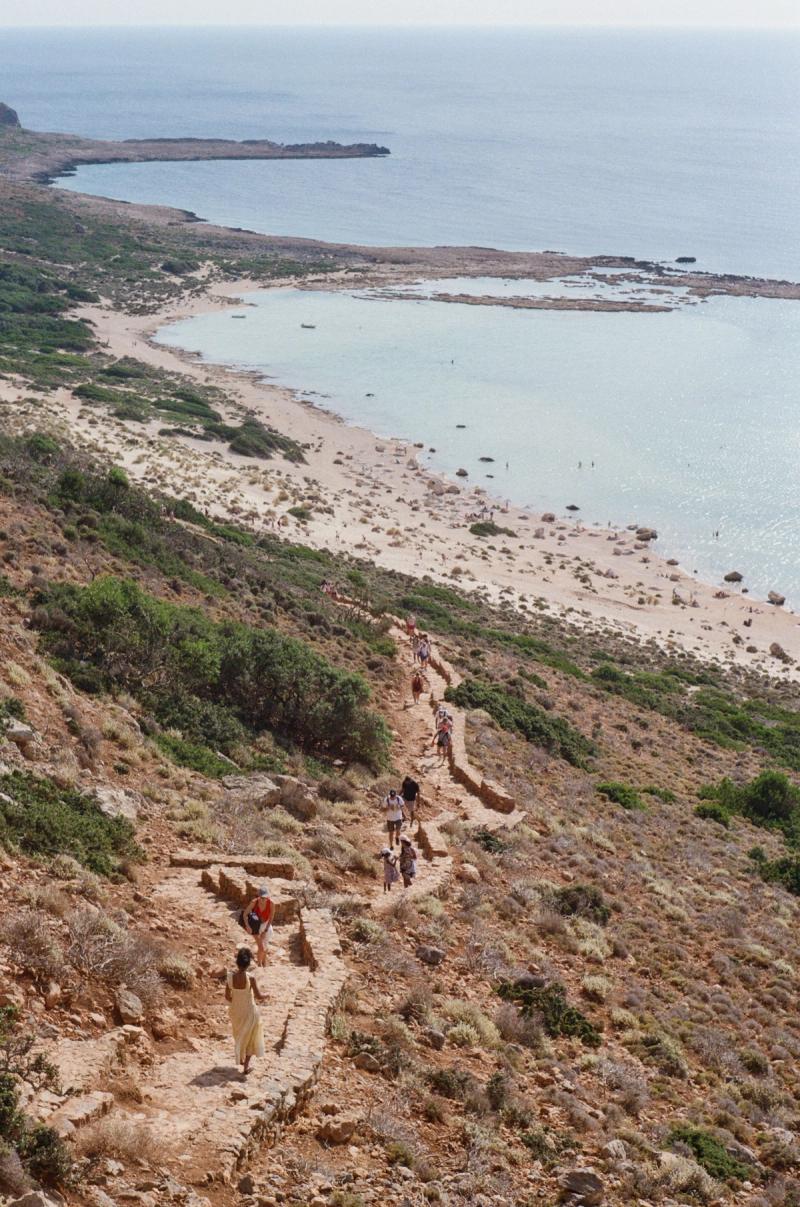 A group of hikers walk down a steep path towards the beach.