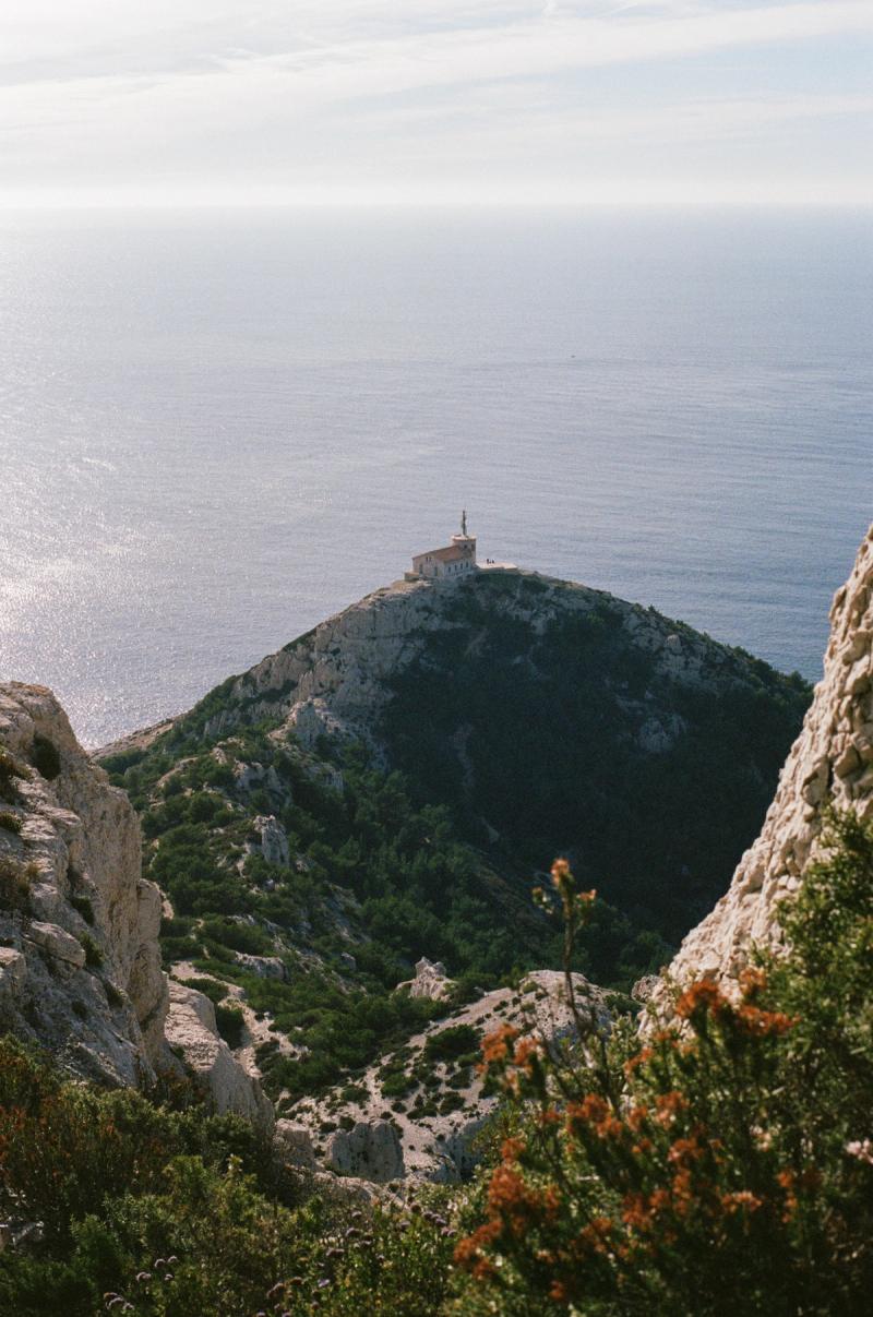 A church on a hill with the ocean in the background and a flower-covered hillside in the foreground.
