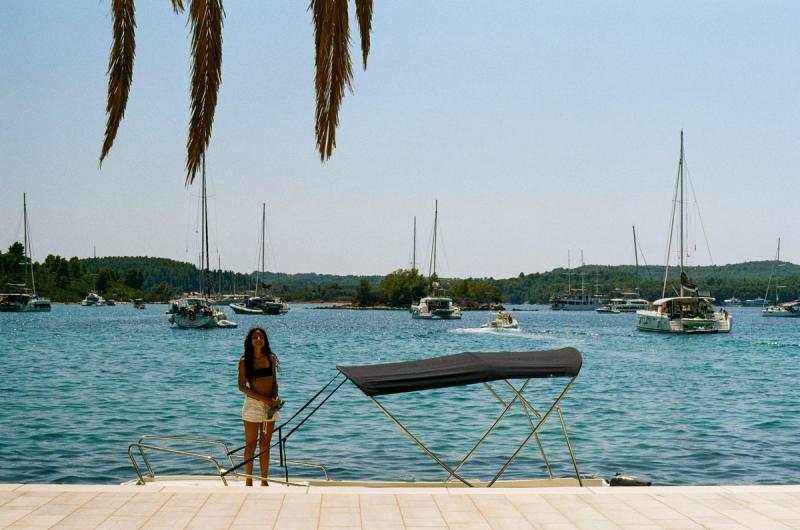 A woman stands on a small motorboat docked in front of several yachts.
