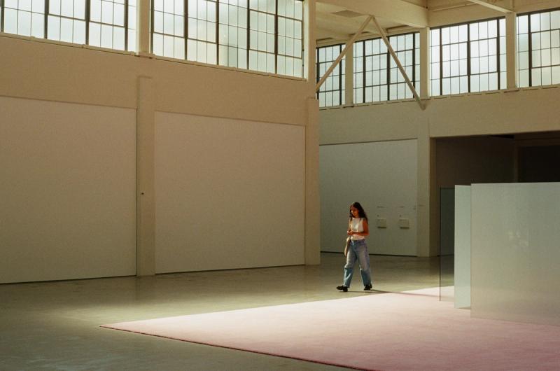A woman walks alongside a pink carpet, in an industrial building.