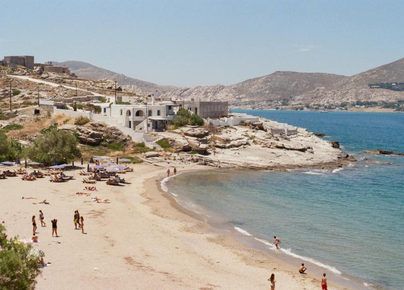 An S-shaped beach curves through the frame, with a modern house on the point.