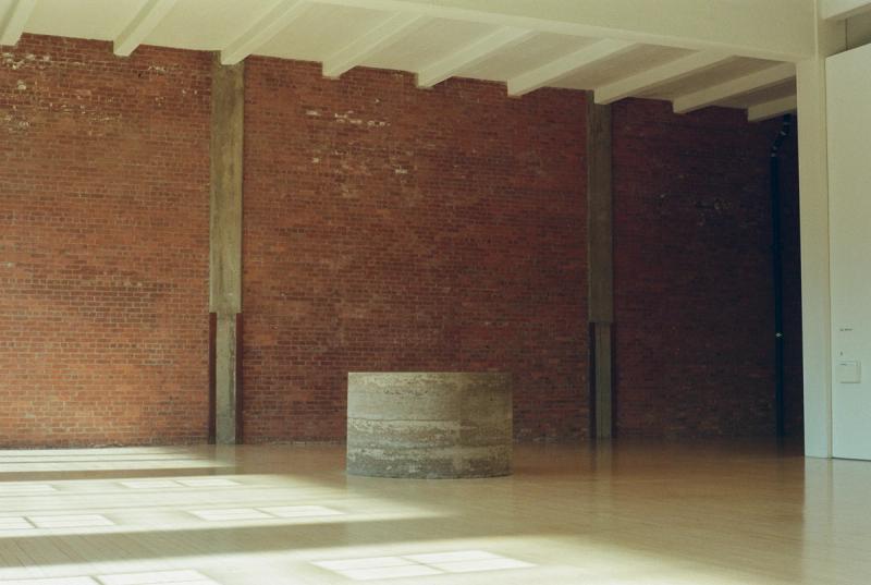 A cement cylinder sits in the center of the frame, backed by a brick wall.