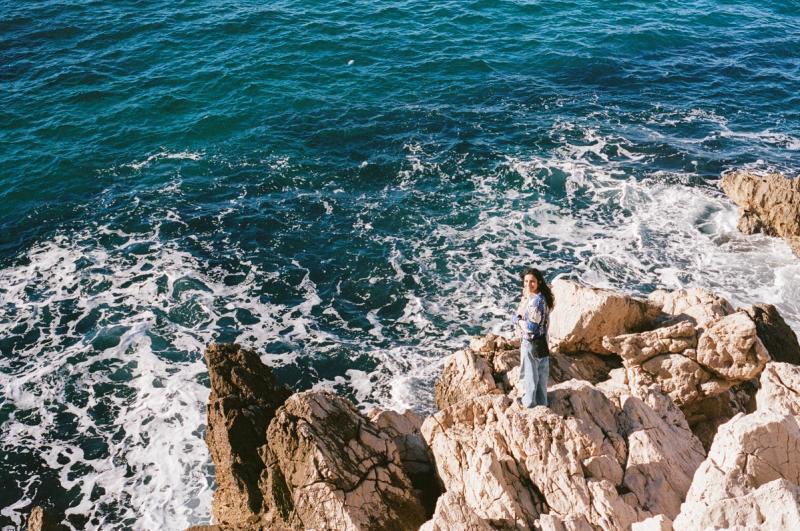 A woman stands on some rocks down at the break zone.