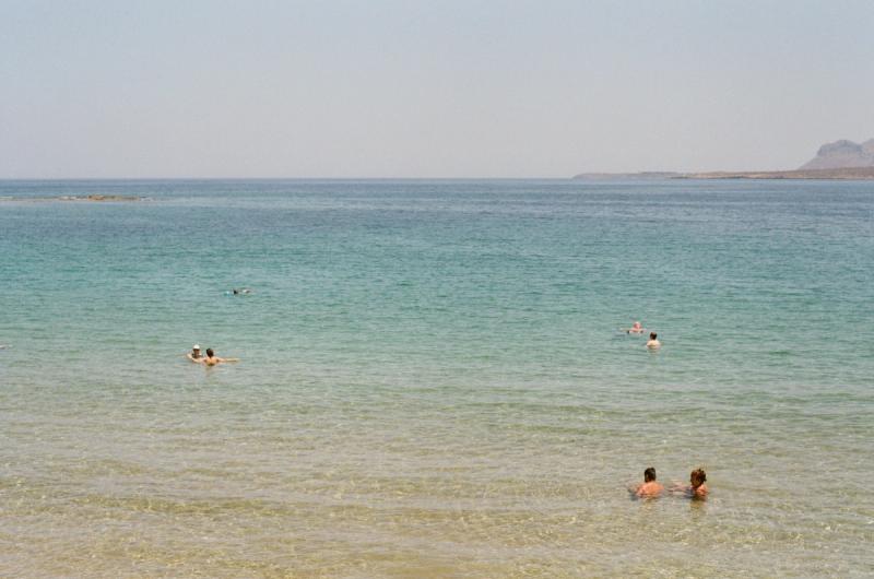A few beachgoers float in a calm sea.