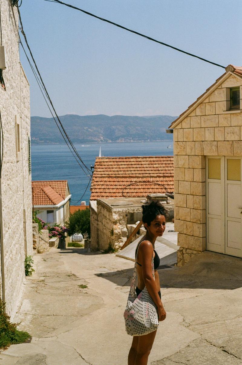 A woman with a bag stands on a narrow road down to the beach.