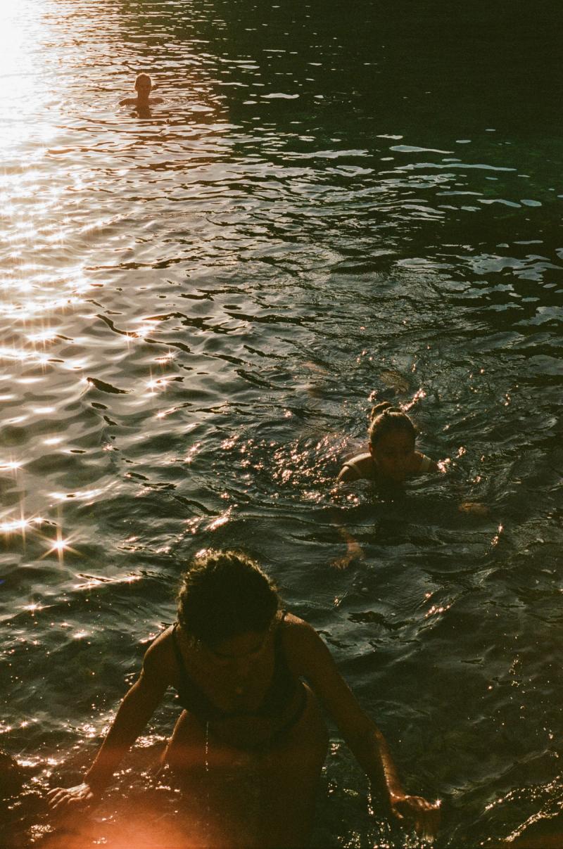 One woman emerges from the water in a bikini, while 2 others swim in behind her.