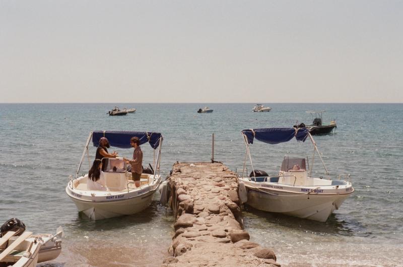 Two men talk while standing in a small boat alongside a stone dock.